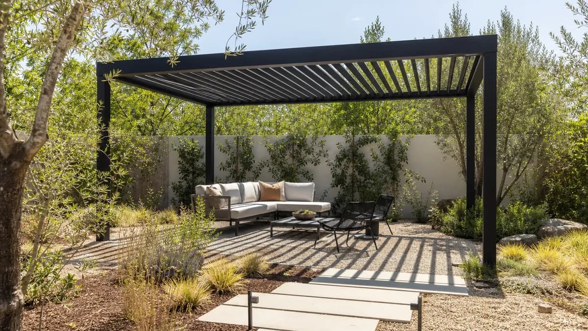 Black steel freestanding pergola over gravel and pavers with olive trees in the background