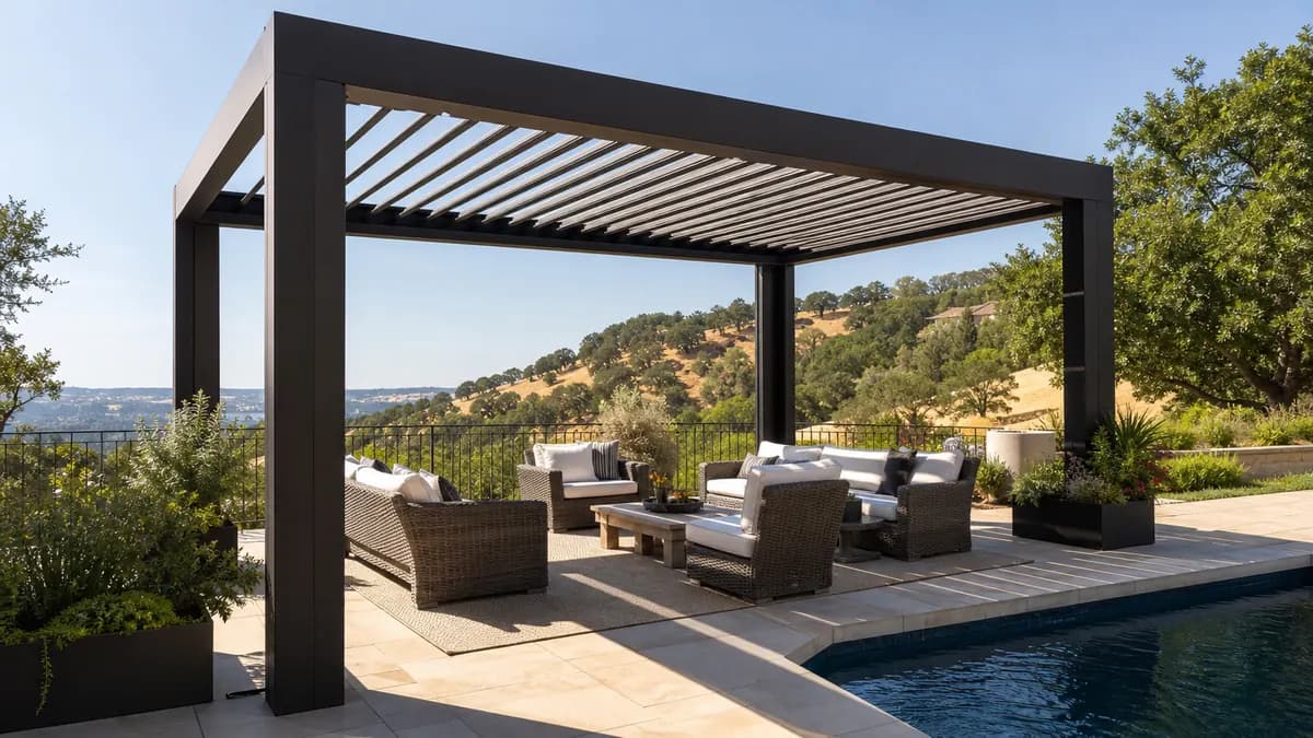 Dark bronze freestanding louvered pergola with adjustable roof blades beside a swimming pool and oak-covered hills